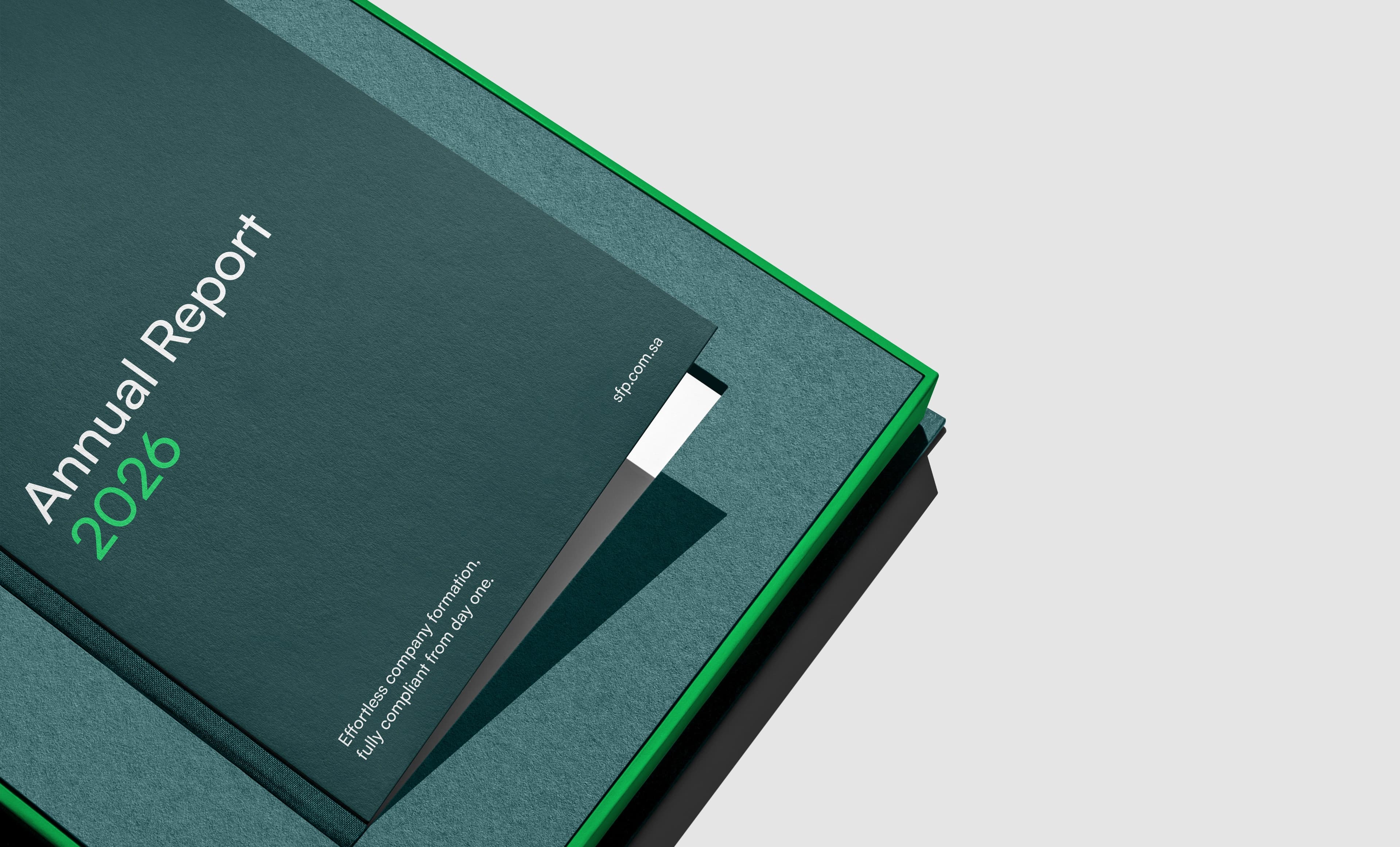A tight corner crop of a dark teal Annual Report 2026 hardcover resting on a teal slipcase with a bright green rim, the year set in green beside a white bookmark ribbon, with the title running off the left edge of the frame.
