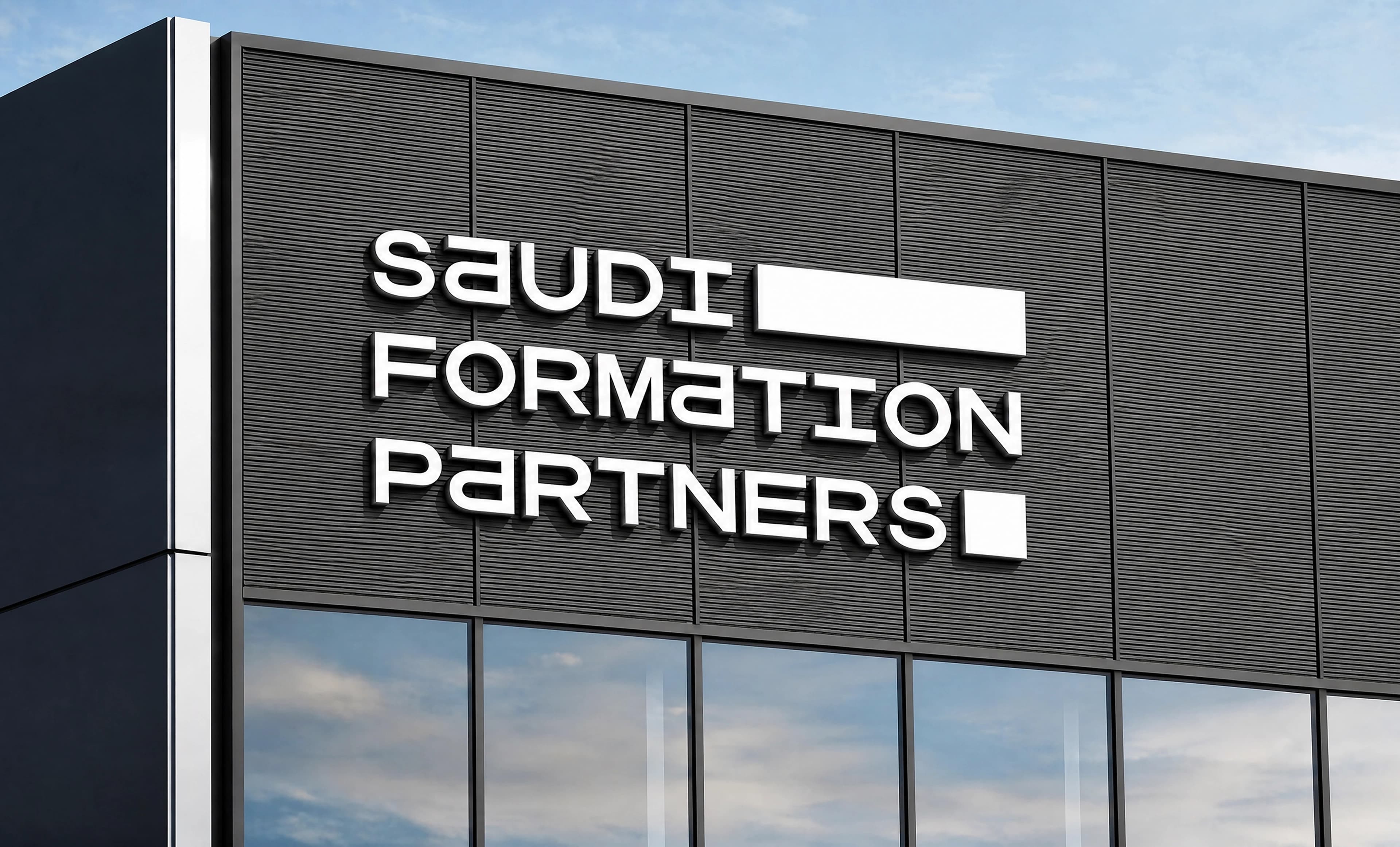 The corner of an office building clad in dark ribbed panels, photographed from below against a blue daylight sky, with large white dimensional Saudi Formation Partners lettering mounted across the facade above the glazing.