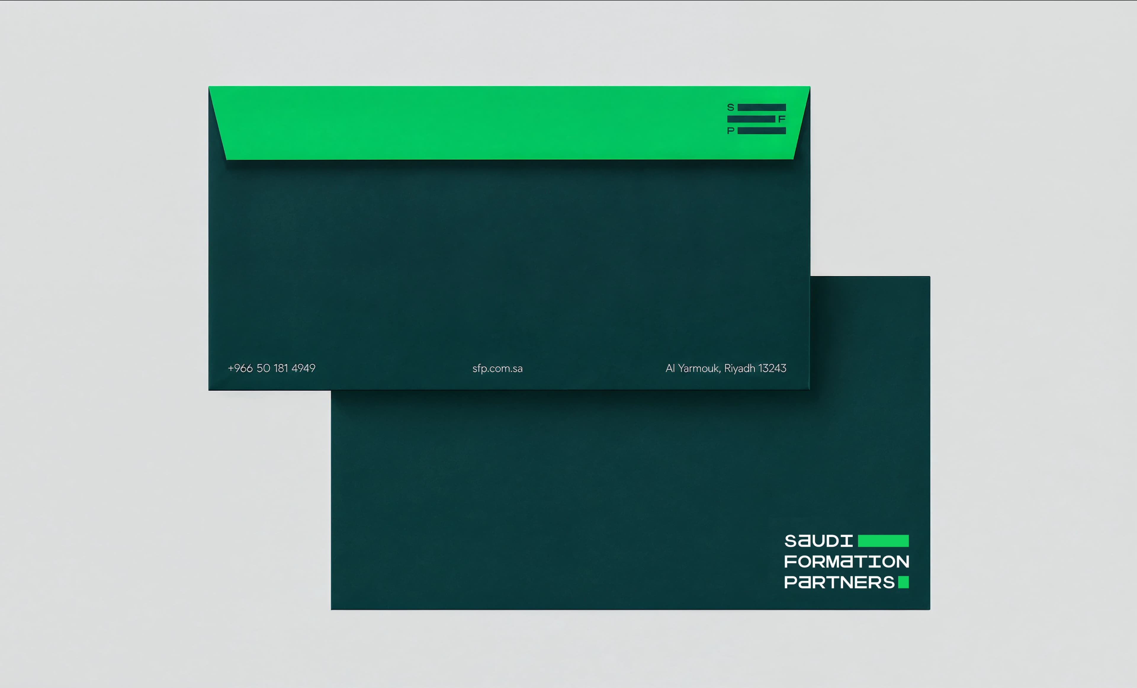 Two dark teal envelopes on a pale neutral ground, one face up with a malachite green flap and a line of contact details along its foot, the other showing the Saudi Formation Partners wordmark, with a printed card beside them.