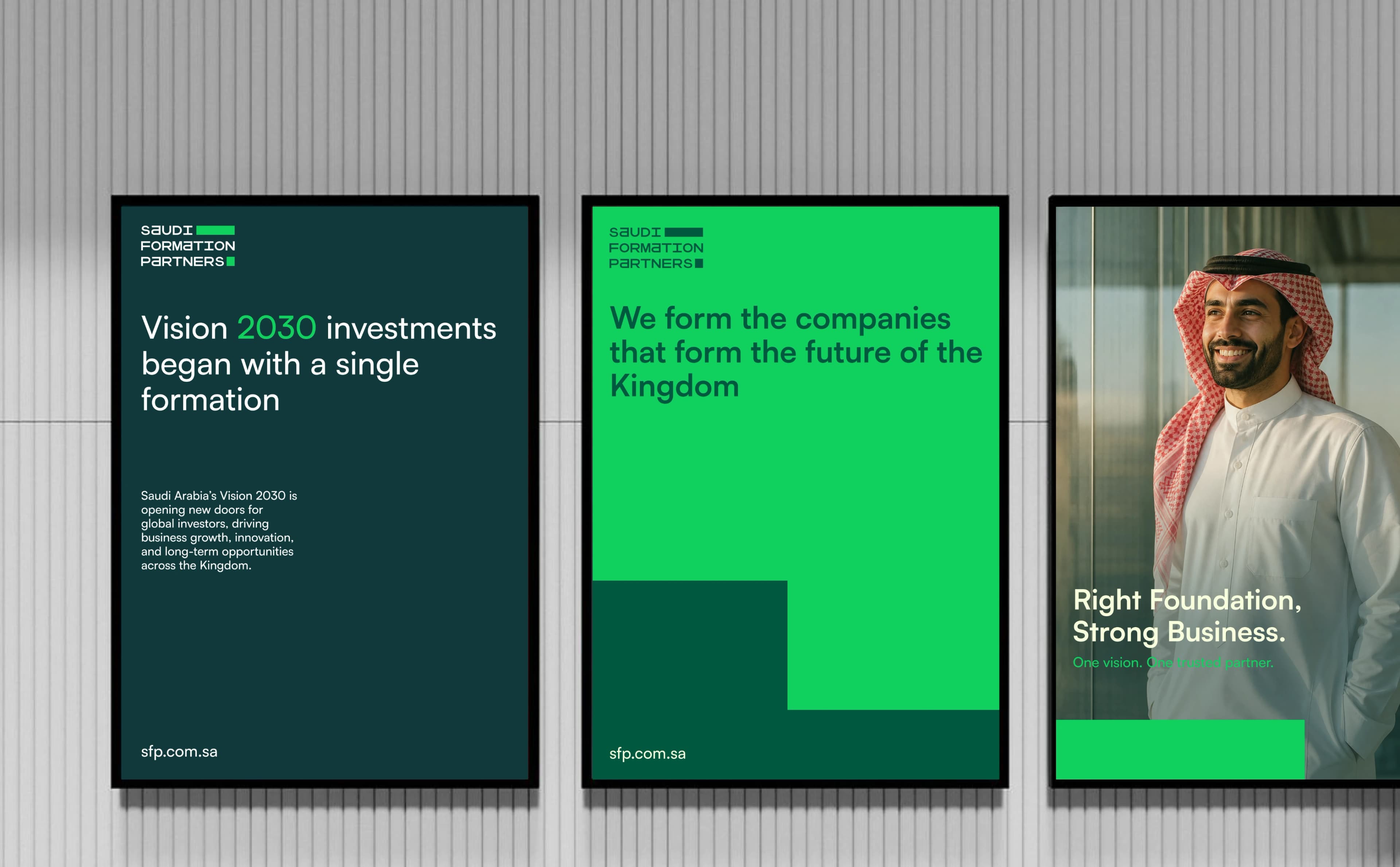 Three black-framed posters mounted side by side on a pale ribbed wall: a dark teal Vision 2030 poster, a bright green poster reading that the company forms the companies that form the future of the Kingdom, and a photographic portrait poster that runs off the right edge of the frame.