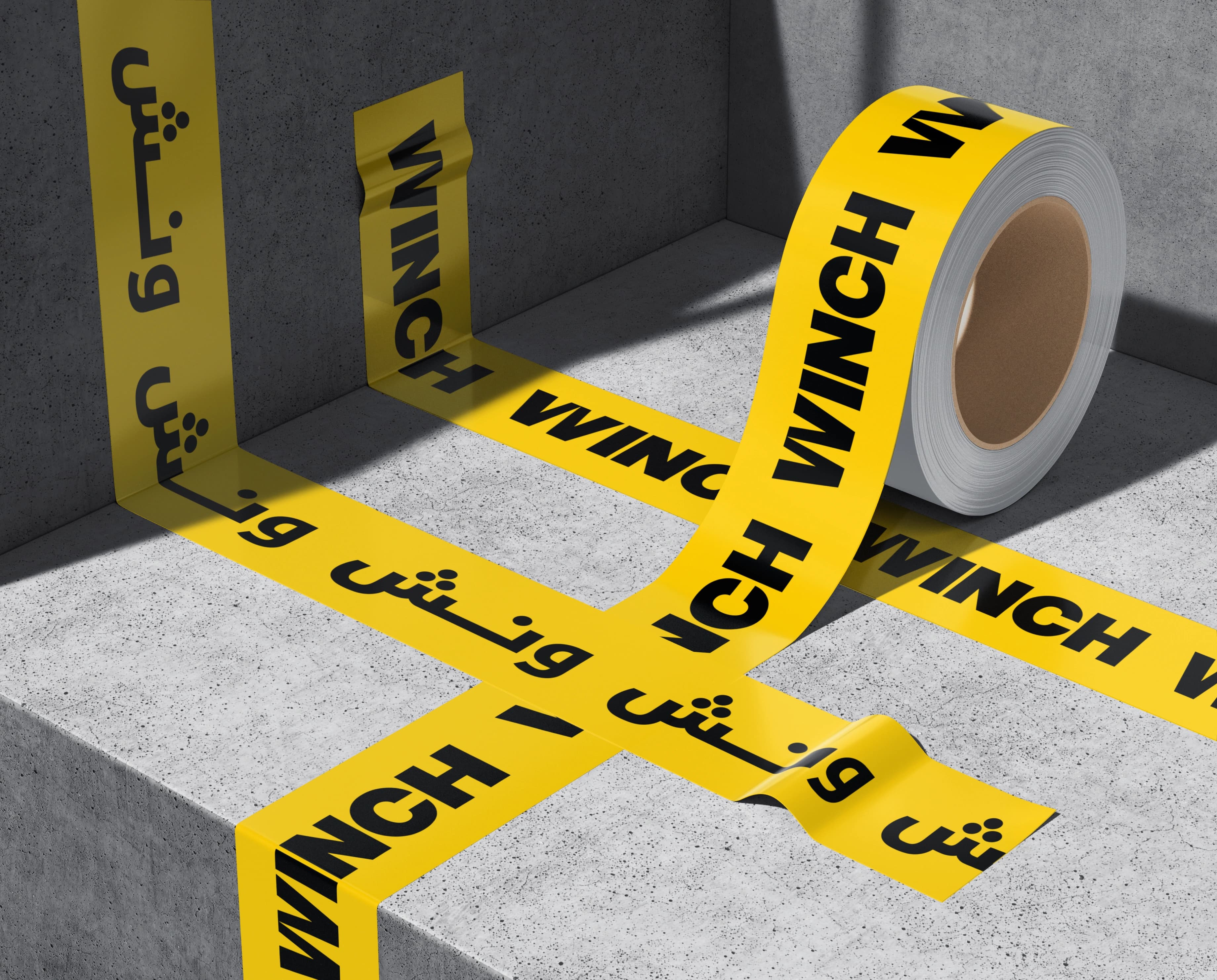 A roll of yellow WINCH barricade tape printed with repeating Latin WINCH and Arabic ونش lettering, the tape crossing a grey concrete step in hard sunlight with the roll resting behind it.