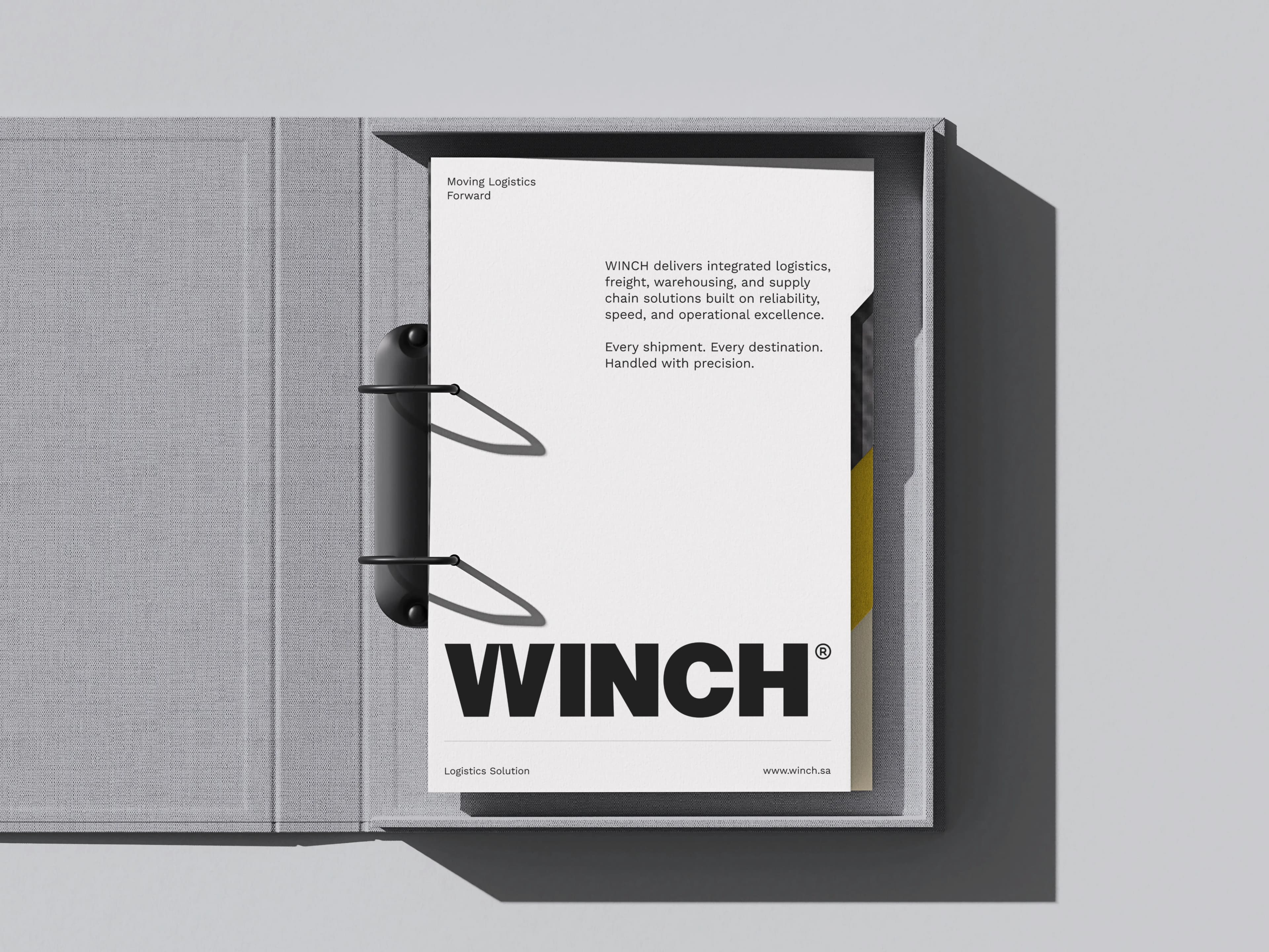 A grey cloth ring binder opened flat on a printed WINCH letterhead sheet headed Moving Logistics Forward, its body copy describing integrated logistics, freight and warehousing services above the WINCH wordmark and the footer Logistics Solution and www.winch.sa.