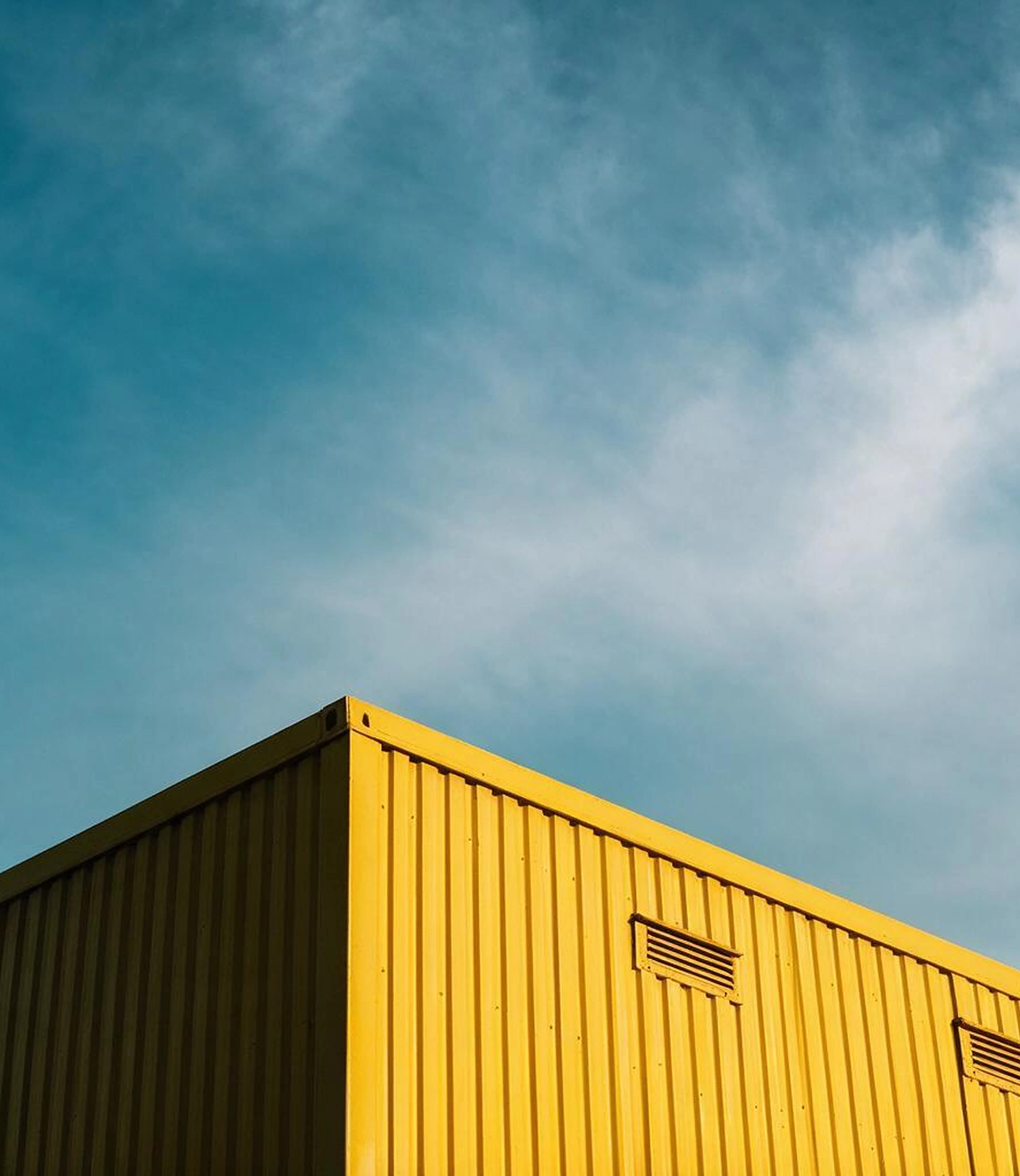 A corrugated yellow shipping container photographed close against a hazy blue-grey sky, carrying the bilingual WINCH lockup reversed in white across its face.