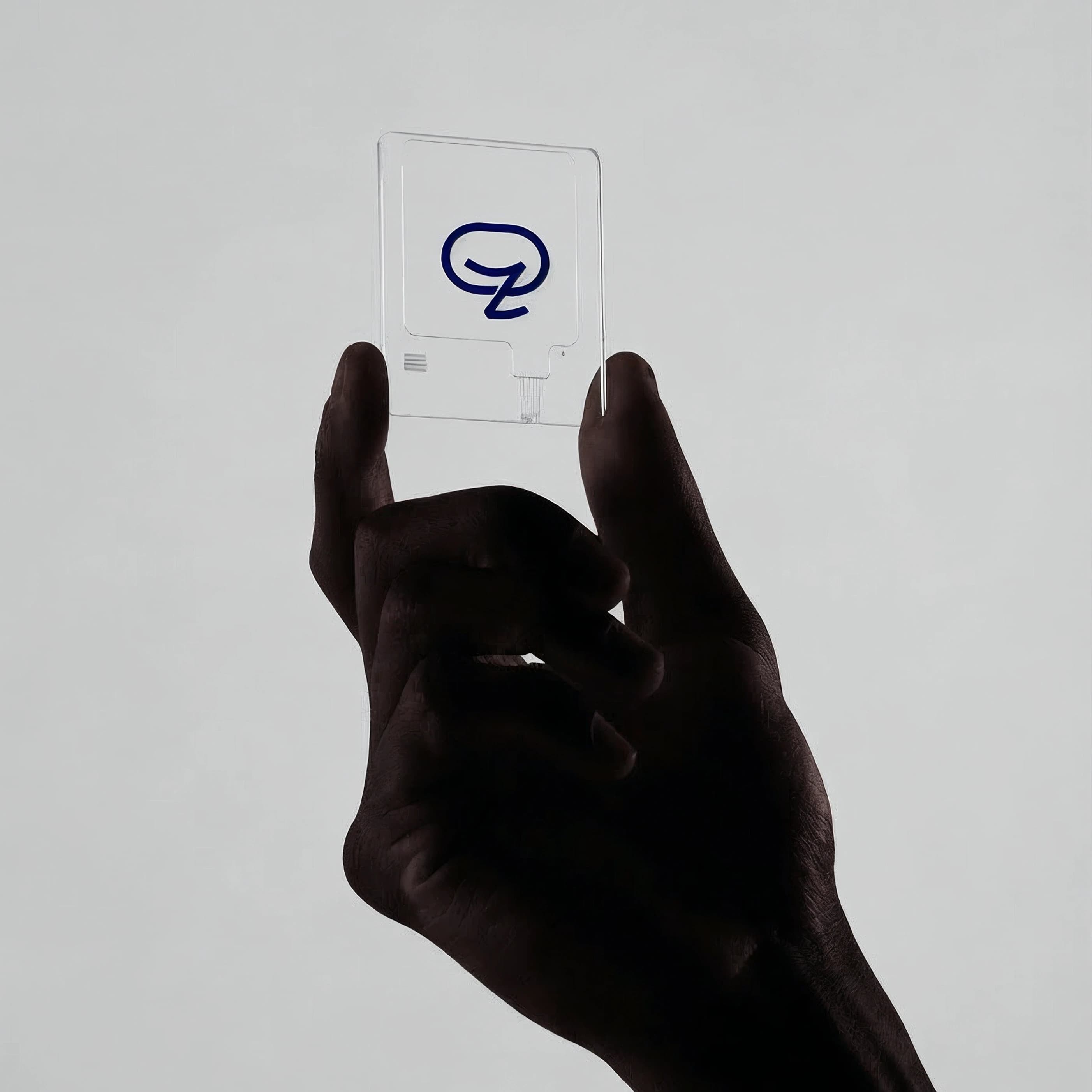 Zakichat — translucent access card A hand entering from below holds a translucent frosted acrylic card embossed with the navy Zakichat mark against a pale grey studio sweep.